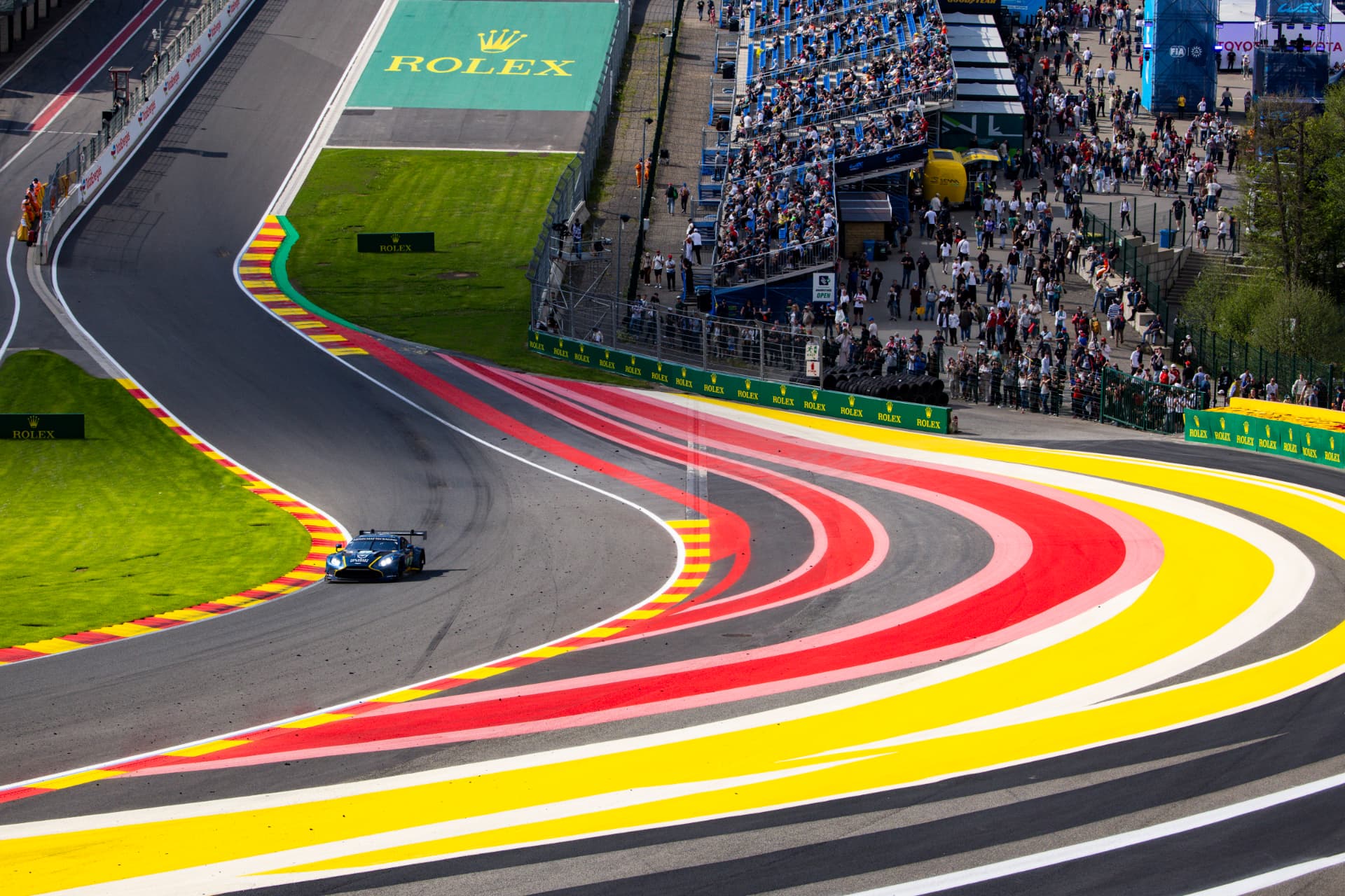 A GT car through the painted red-and-yellow kerbs of Eau Rouge with spectators above.