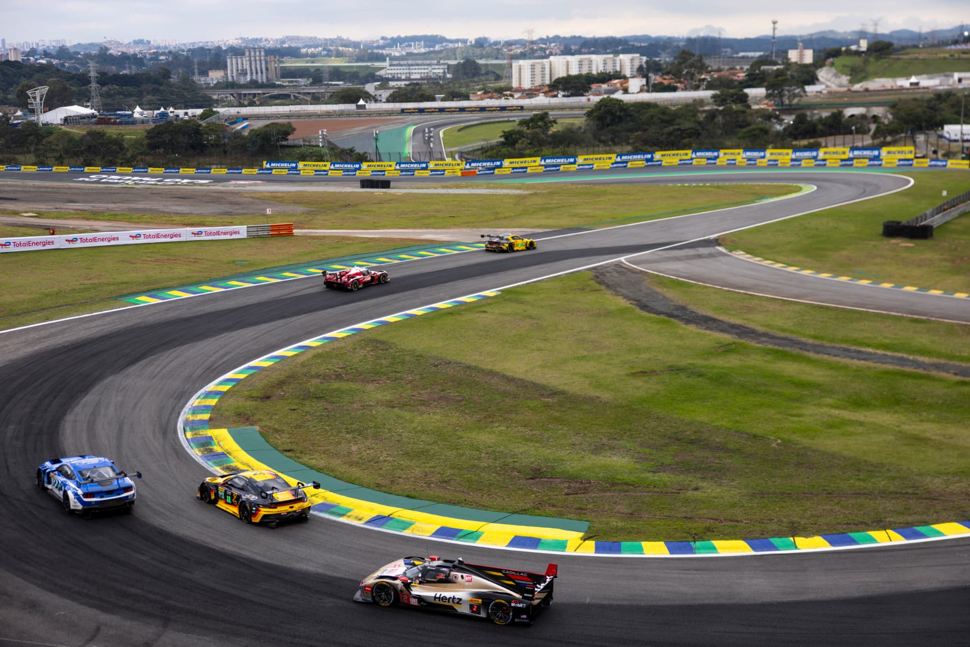 Hypercars and LMGT3 cars through the Interlagos infield with São Paulo in the background.