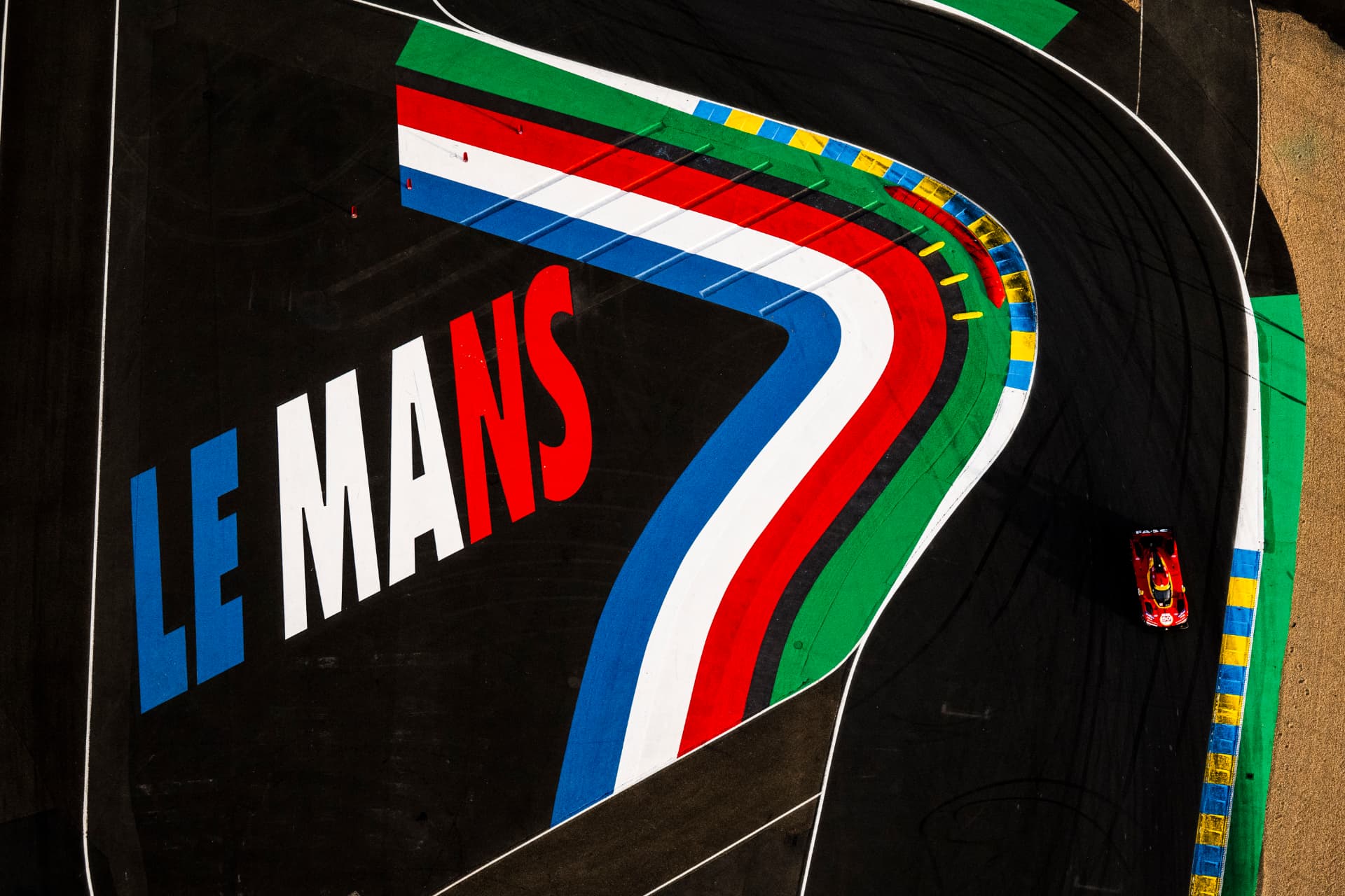 Aerial view of a Hypercar over the Le Mans track paint and kerbs.