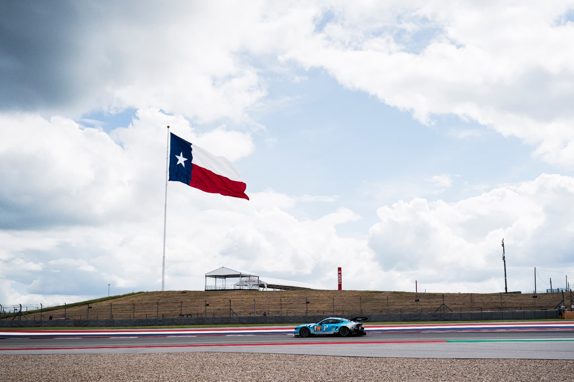 A LMGT3 car on the back straight at Circuit of the Americas with the Texas flag flying.