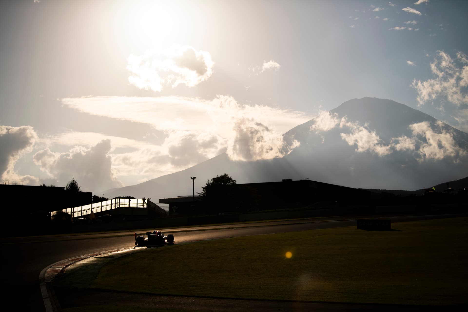 A Hypercar in silhouette against low sun and clouds at Fuji Speedway.